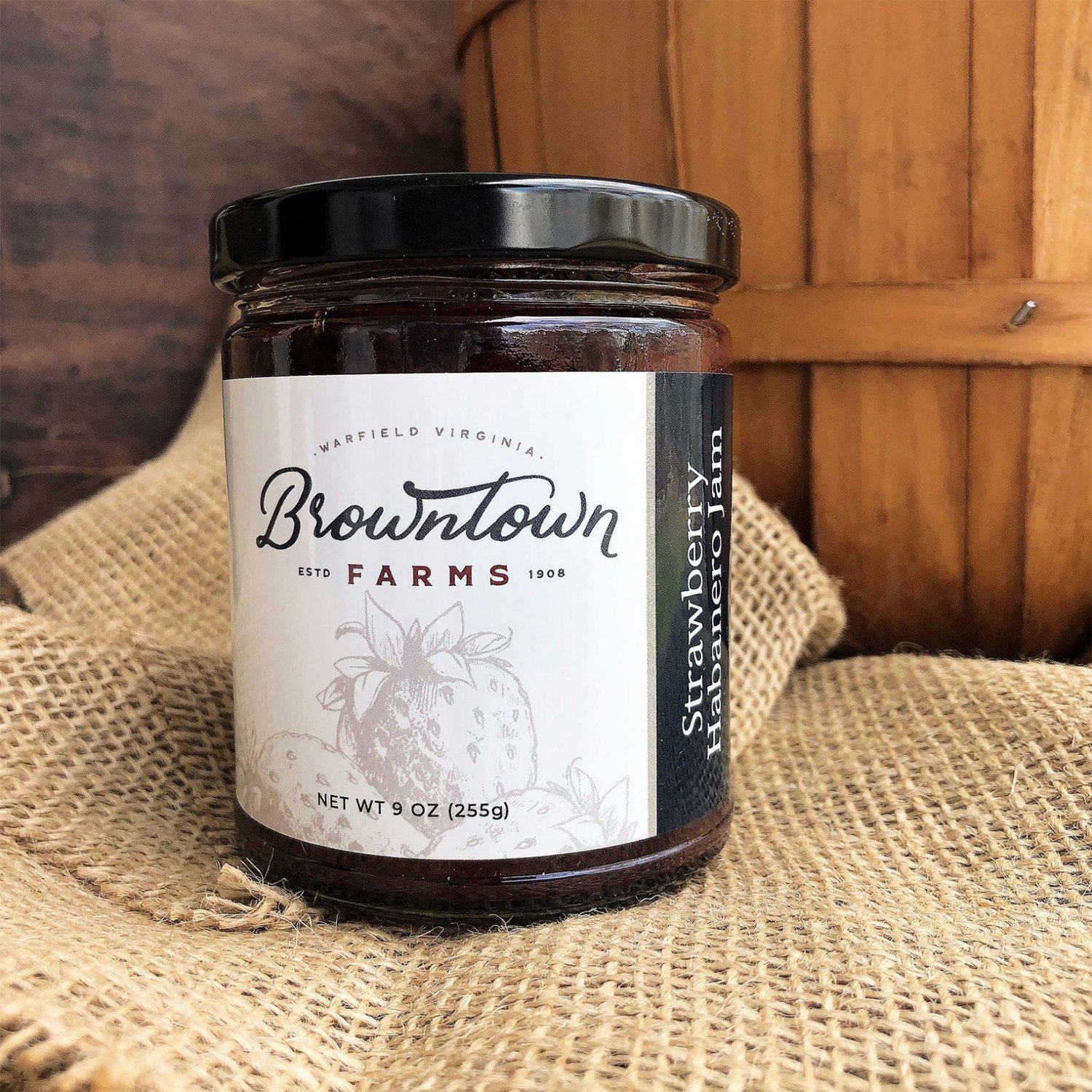 Browntown+Farms+-+Virginia+-+BTF-Strawberry-Habanero-Jam Jar of Browntown Farms Strawberry Habanero Jam, 9 oz, featuring a rustic design with a wooden background and burlap texture, highlighting the brand's Virginia heritage since 1908.